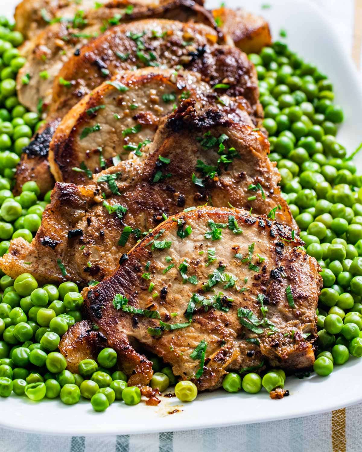 sideview shot of lemon garlic pork chops on a white serving platter with a side of peas