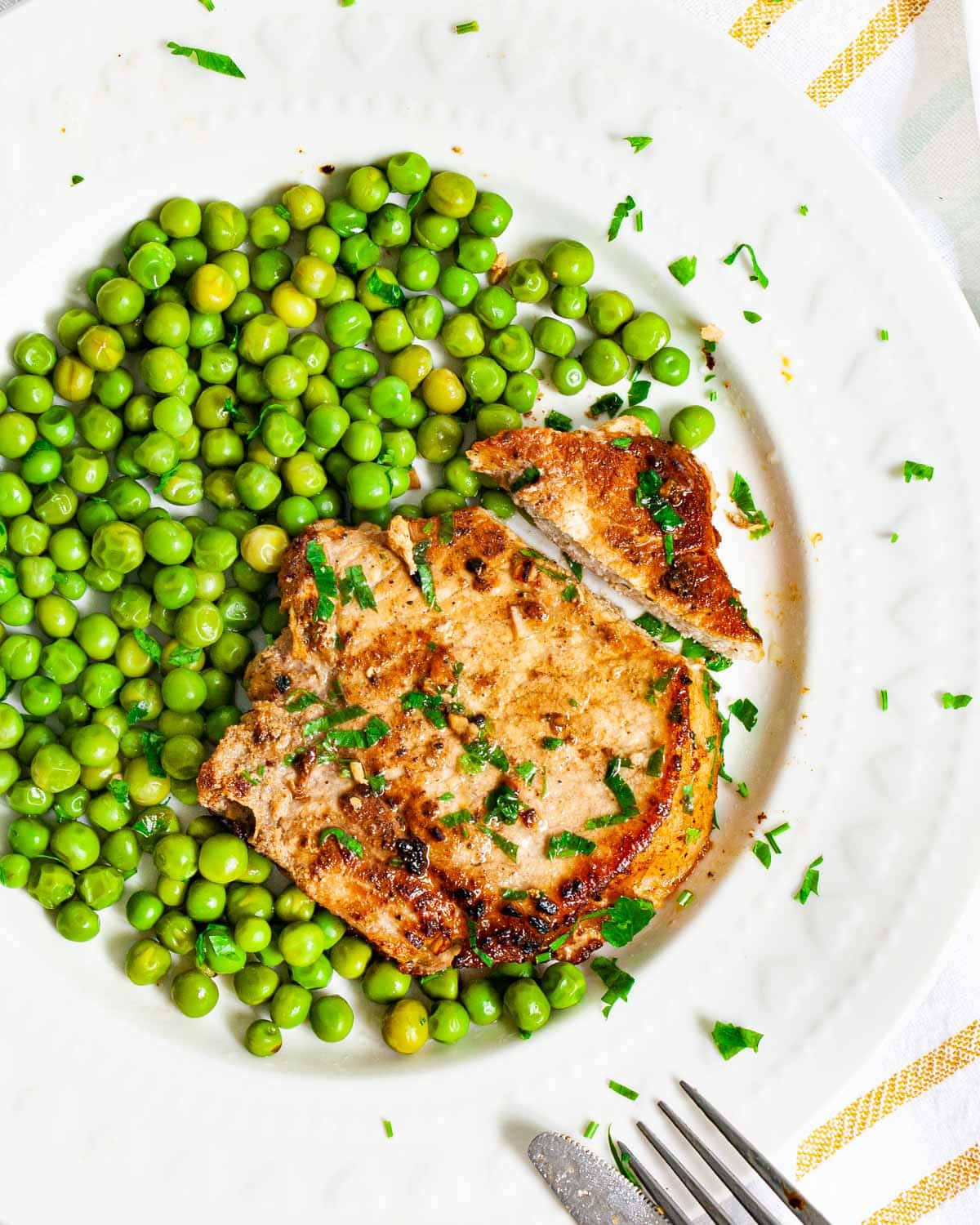 overhead shot of a pork chop on a white plate with a side of peas