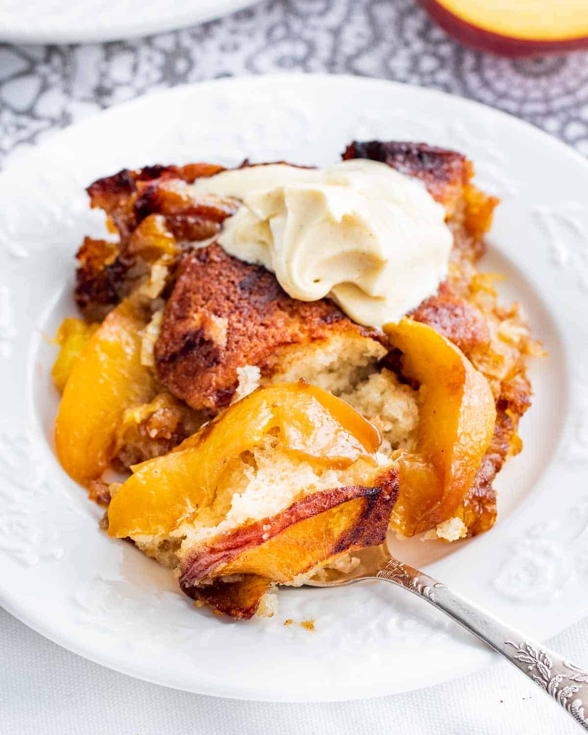 a piece of peach cobbler with a scoop of vanilla ice cream on a white plate with a spoon 