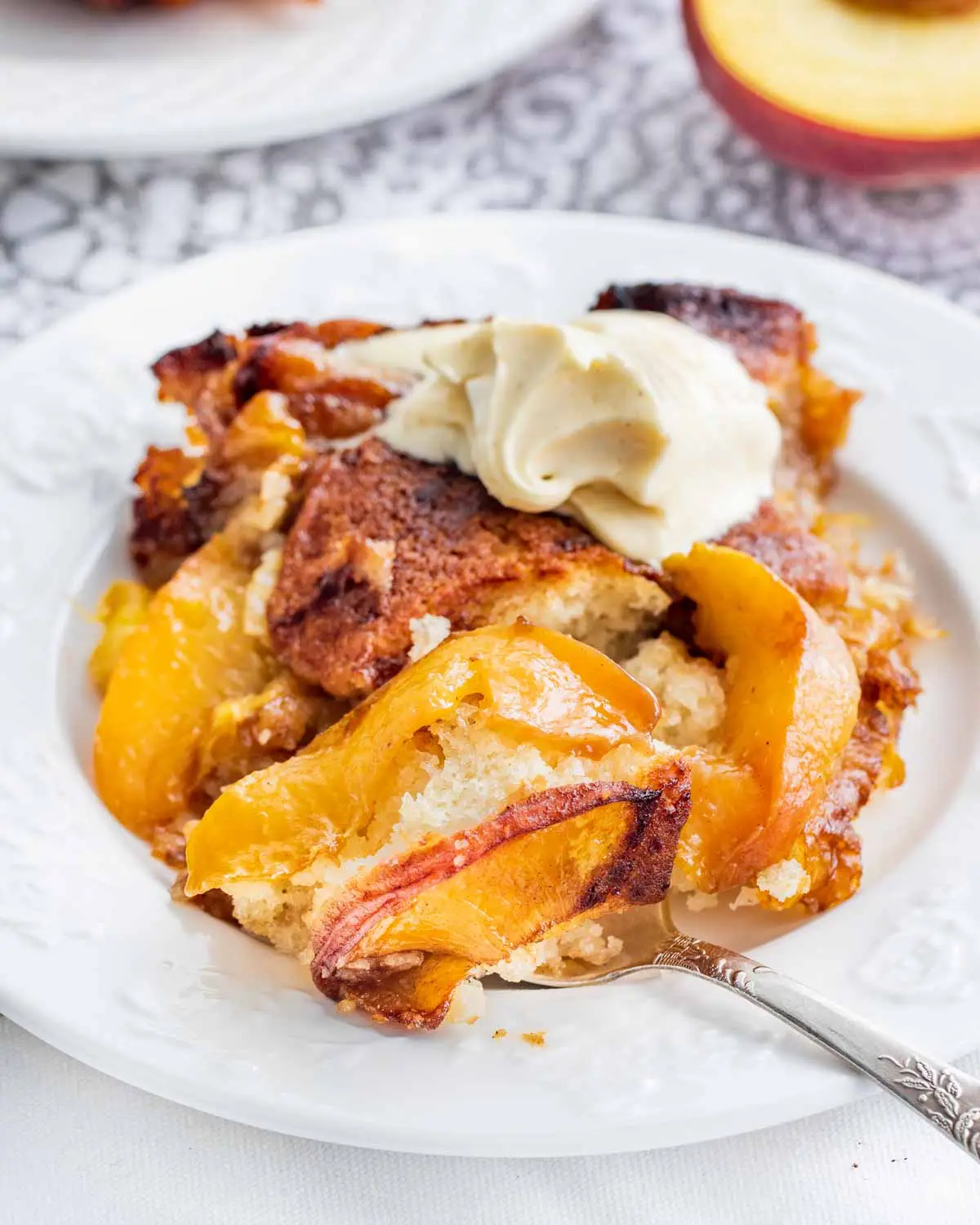 a piece of peach cobbler with a scoop of vanilla ice cream on a white plate with a spoon 