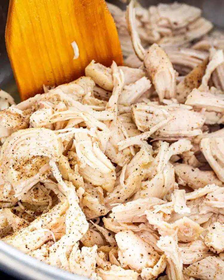 closeup of shredded chicken in the instant pot with a wooden spatula inside