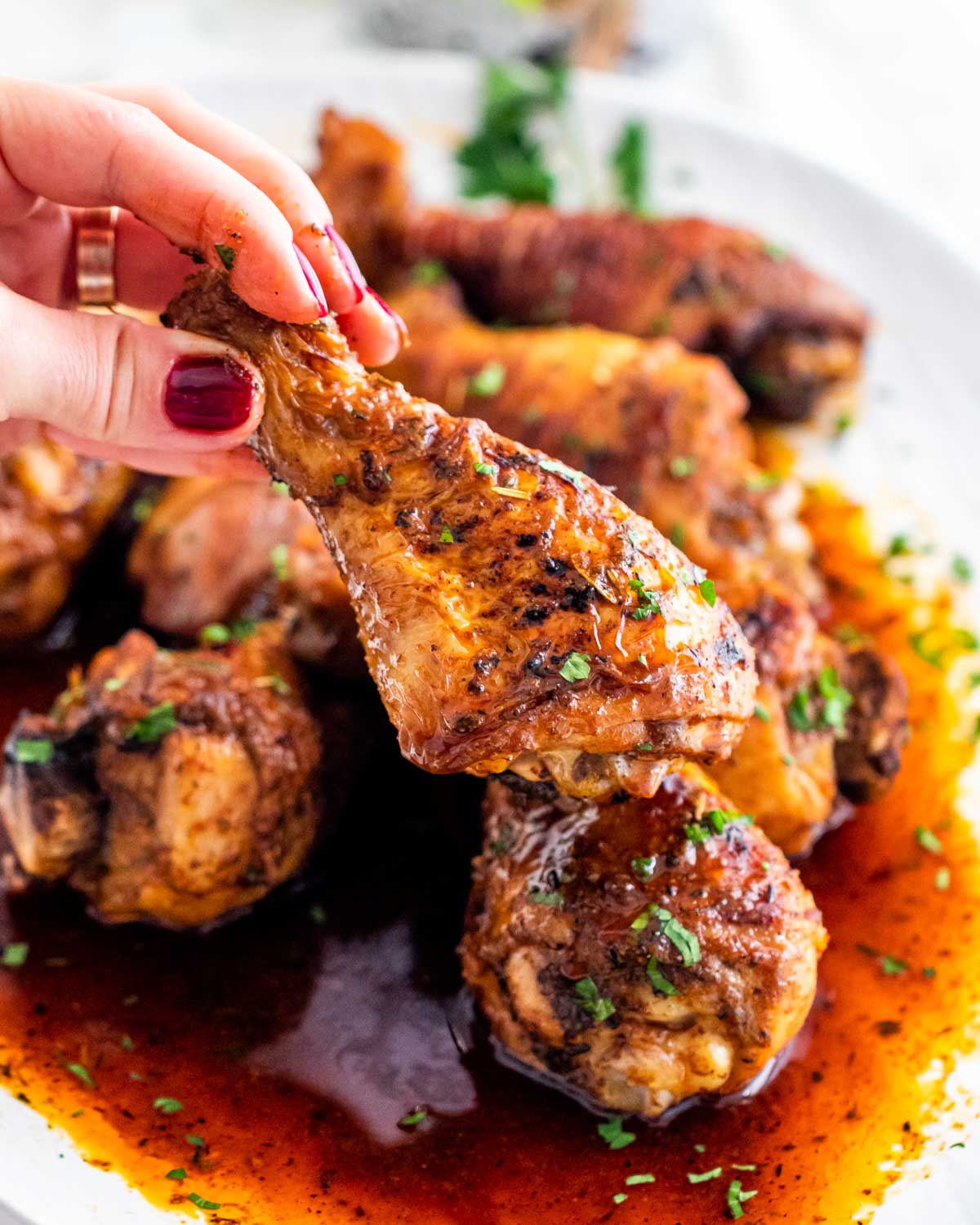 a hand holding an oven baked chicken drumstick above a platter.