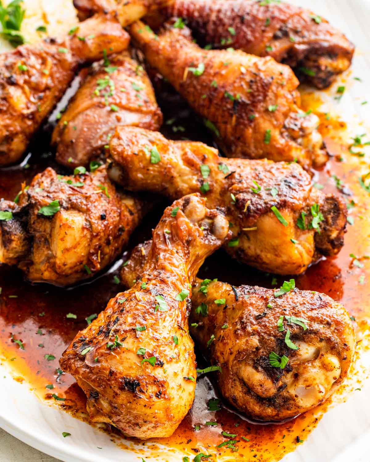 closeup of baked chicken drumsticks on a white serving platter with sauce from pan.