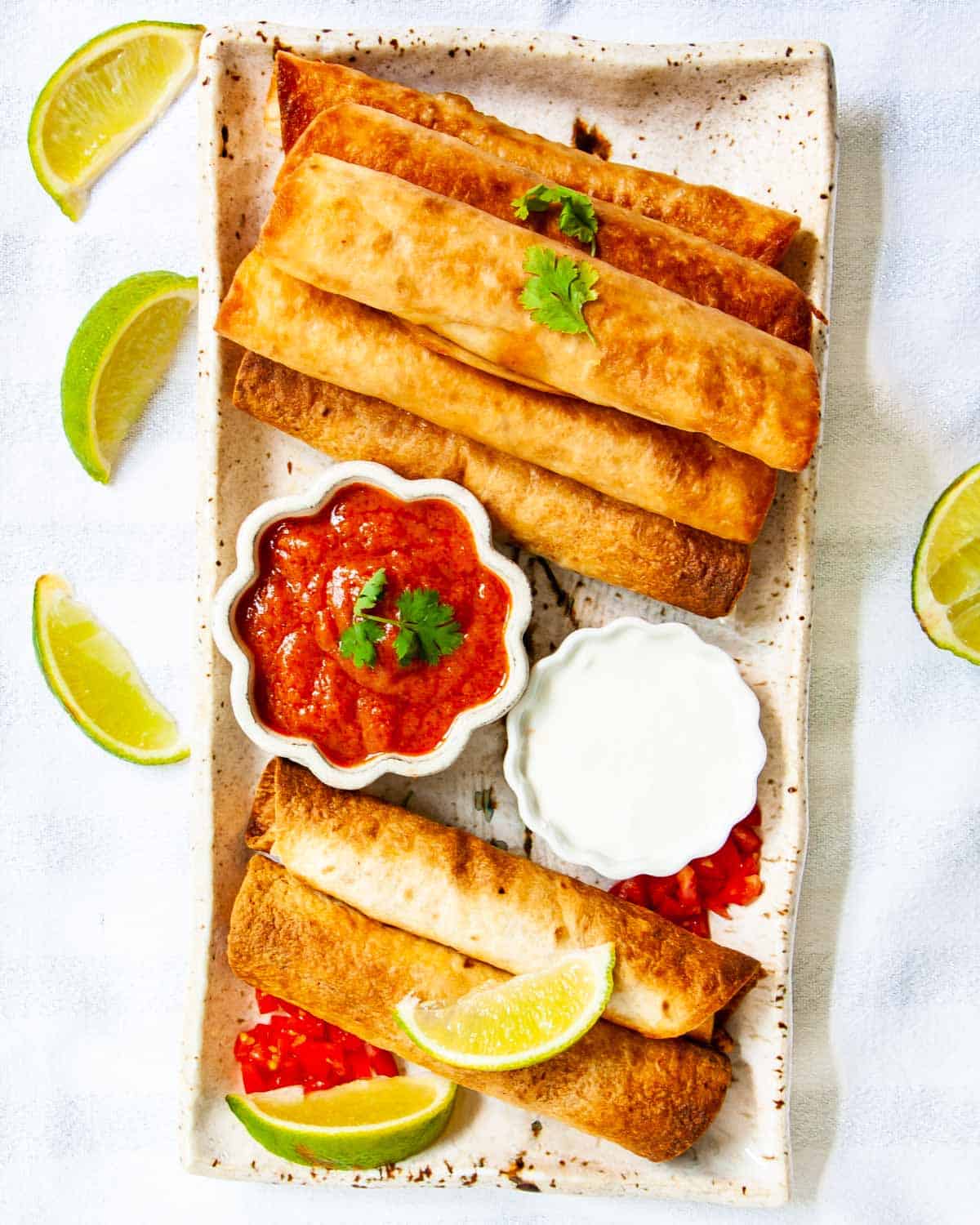 overhead shot of chicken taquitos on a serving platter with salsa and sour cream.