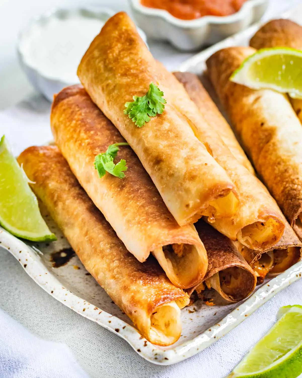 chicken taquitos stacked on top of each other on a serving platter.