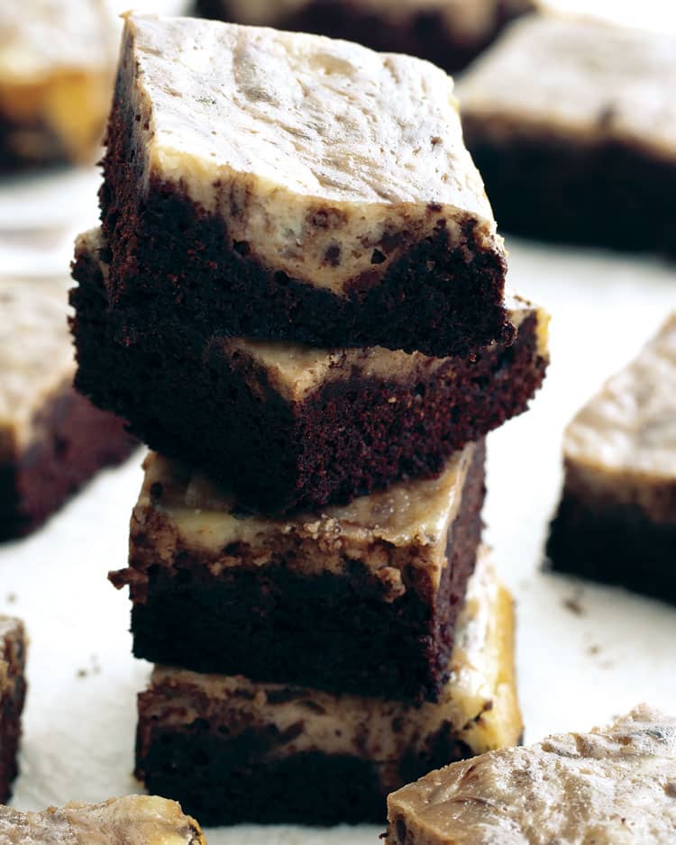 a stack of cream cheese brownies with a few scattered around