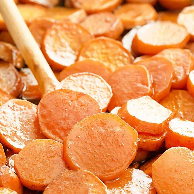 candied yams on a baking sheet with a wooden spoon.