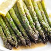 closeup of roasted asparagus on a plate with lemon wedge.