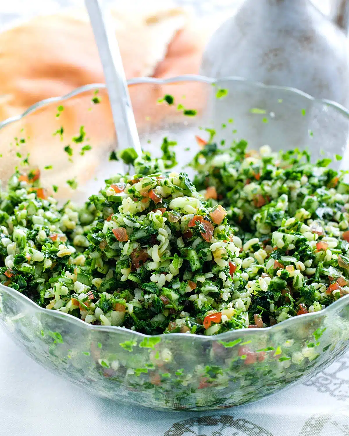 closeup of tabbouleh salad in a glass bowl with a spoon inside.