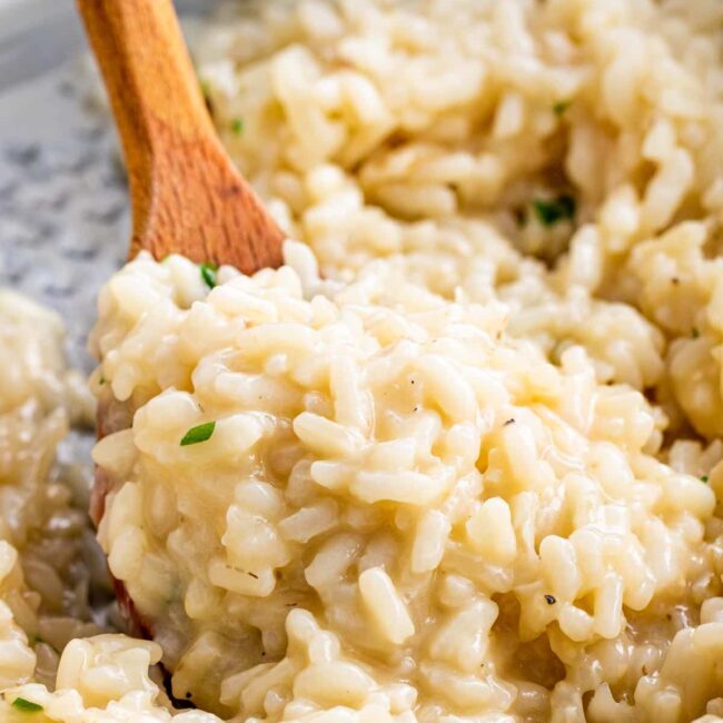 a wooden spoon holding some risotto in a pan.