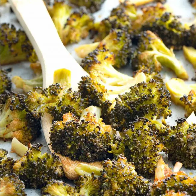closeup shot of roasted broccoli on a serving platter with a serving spoon.