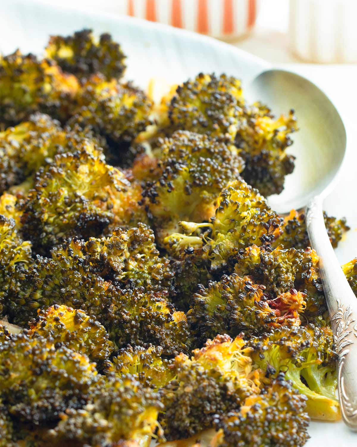 closeup shot of roasted broccoli on a serving platter with a serving spoon.