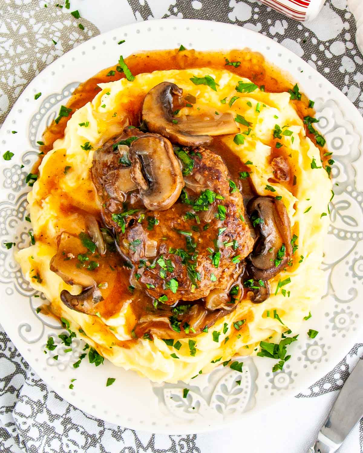 a salisbury steak over a bed of mashed potatoes garnished with parsley.