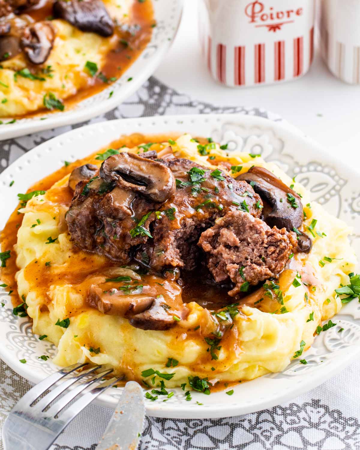 a salisbury steak over a bed of mashed potatoes garnished with parsley.