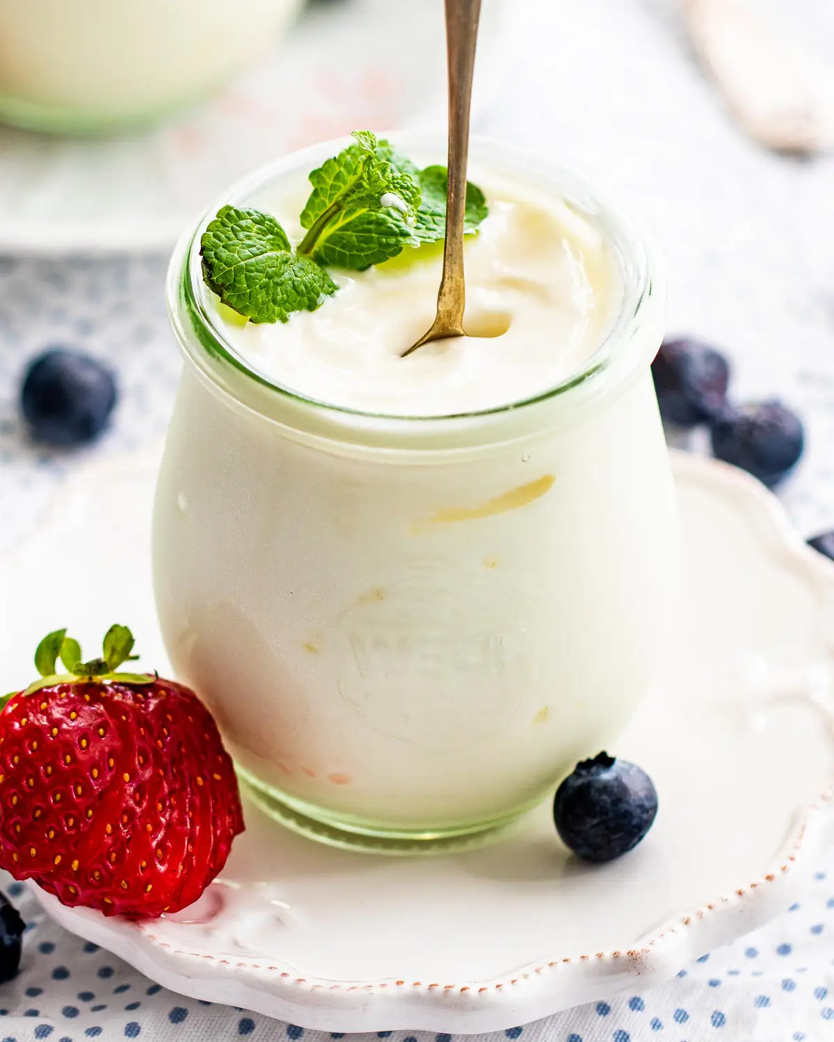 yogurt in a serving jar with a spoon standing garnished with mint and berries.