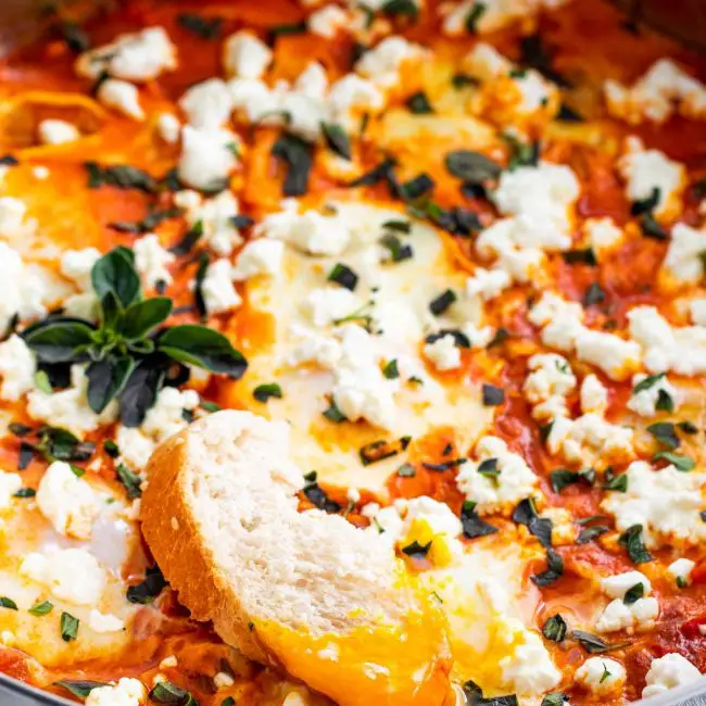 shakshuka in a skillet with a piece of bread dipped in an egg.