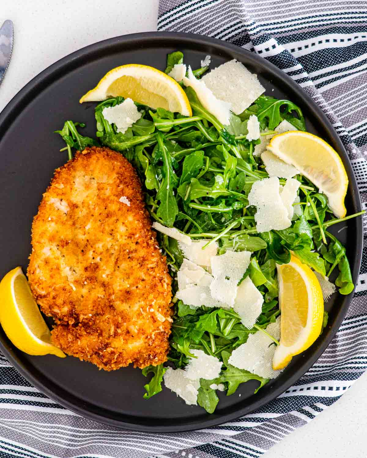 chicken milanese next to arugula salad garnished with shaved parmesan and lemon wedges.