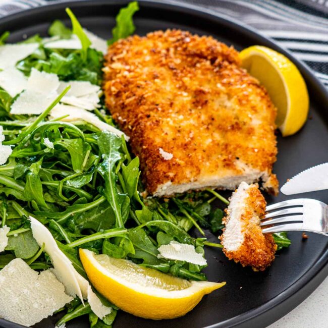 chicken milanese next to arugula salad garnished with shaved parmesan and lemon wedges.