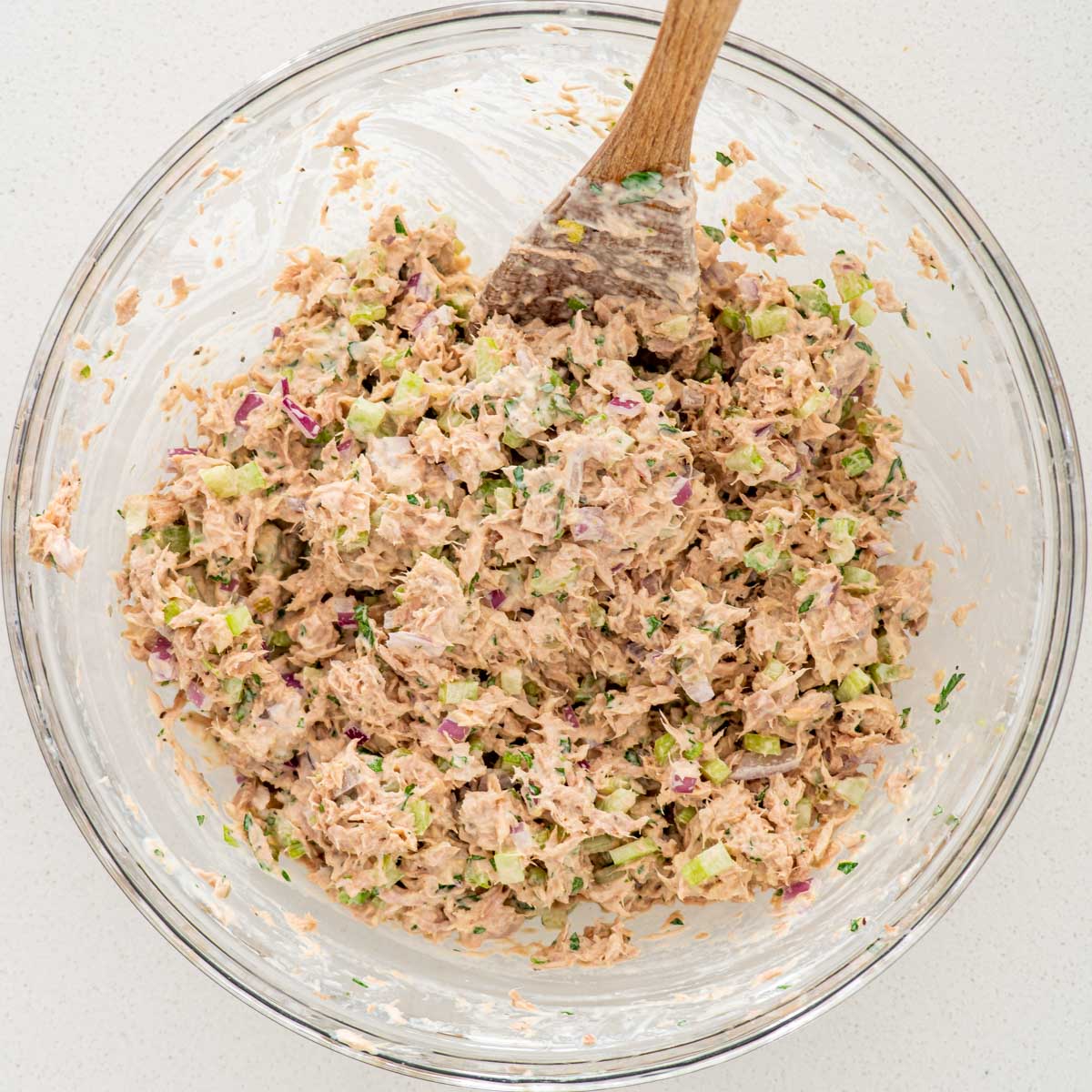 tuna salad in a glass bowl with a wooden mixing spoon.