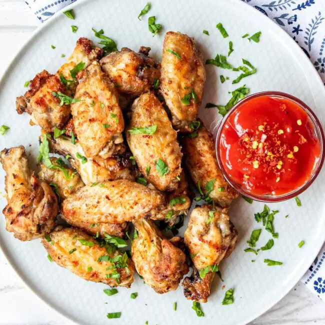 chicken wings on a white plate with hot sauce garnished with parsley.