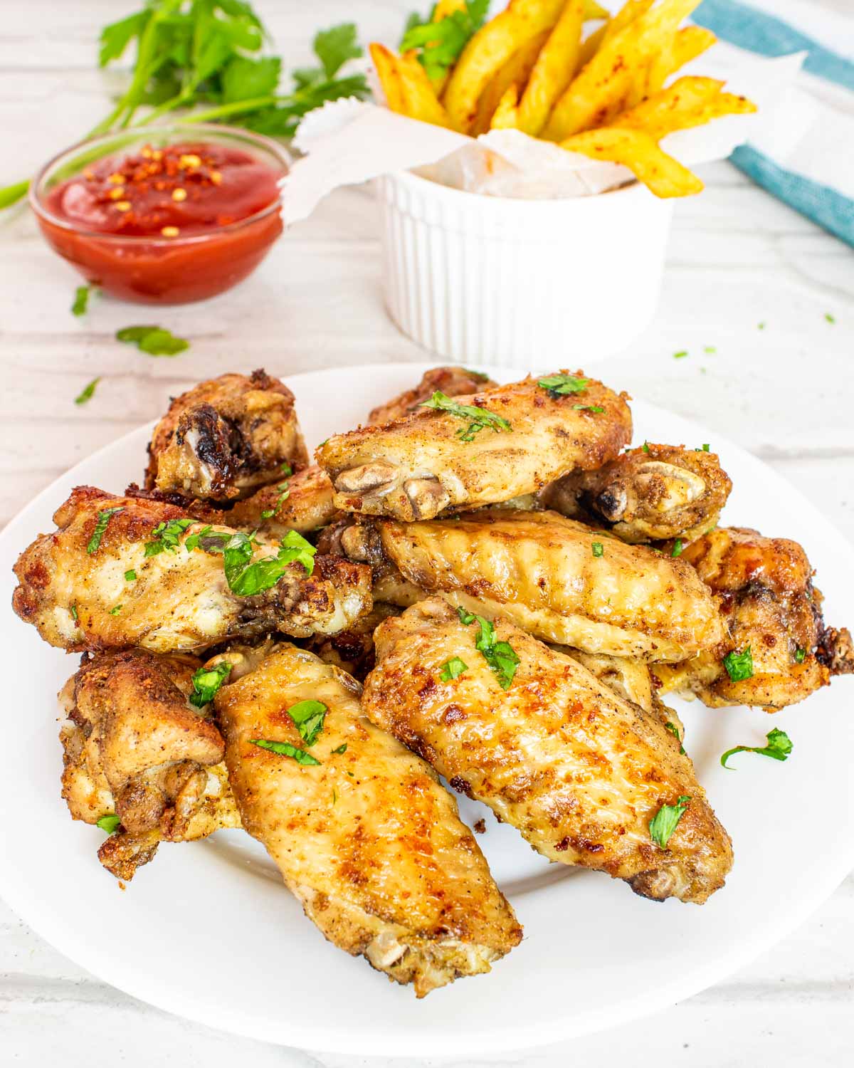 chicken wings on a white plate with french fries in the background.