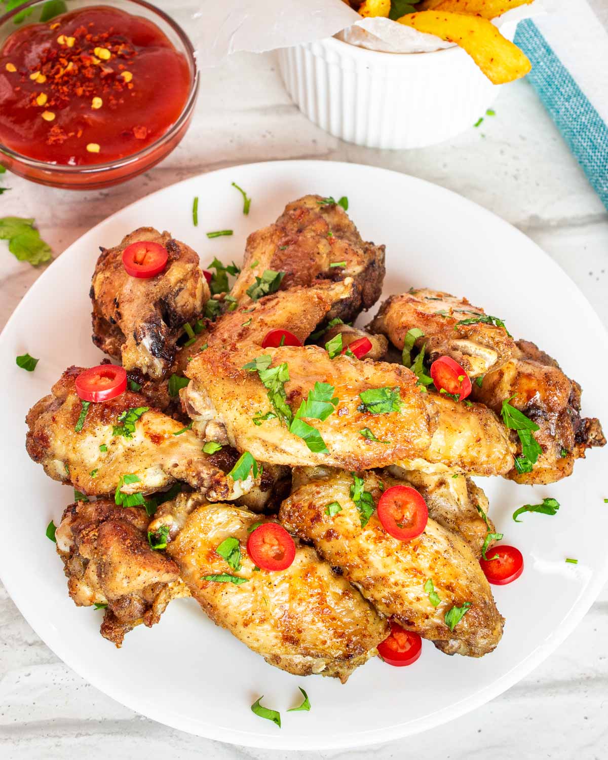 chicken wings on a white plate garnished with parsley and red chili peppers.