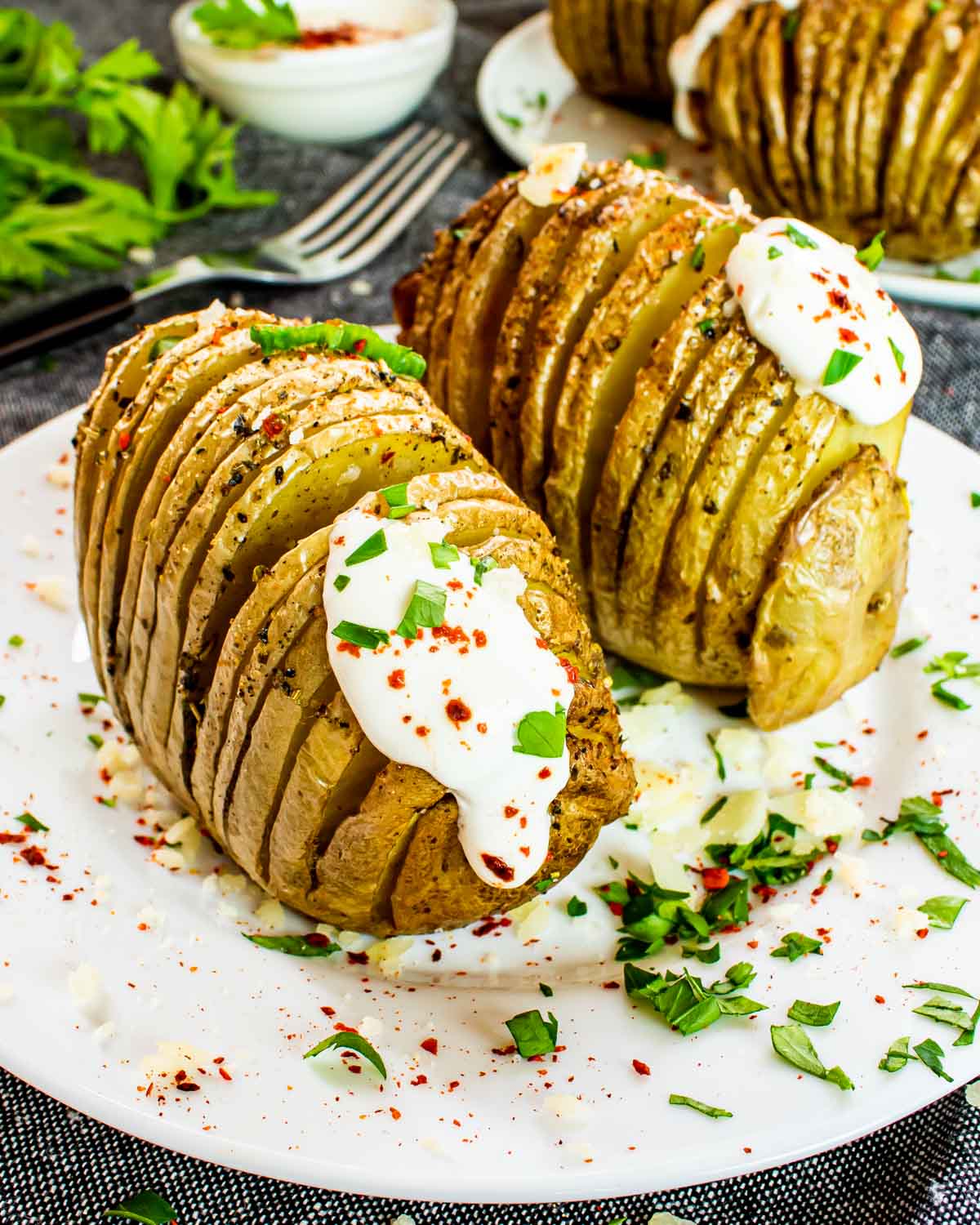 2 hasselback potatoes on a white plate garnished with sour cream and parsley.