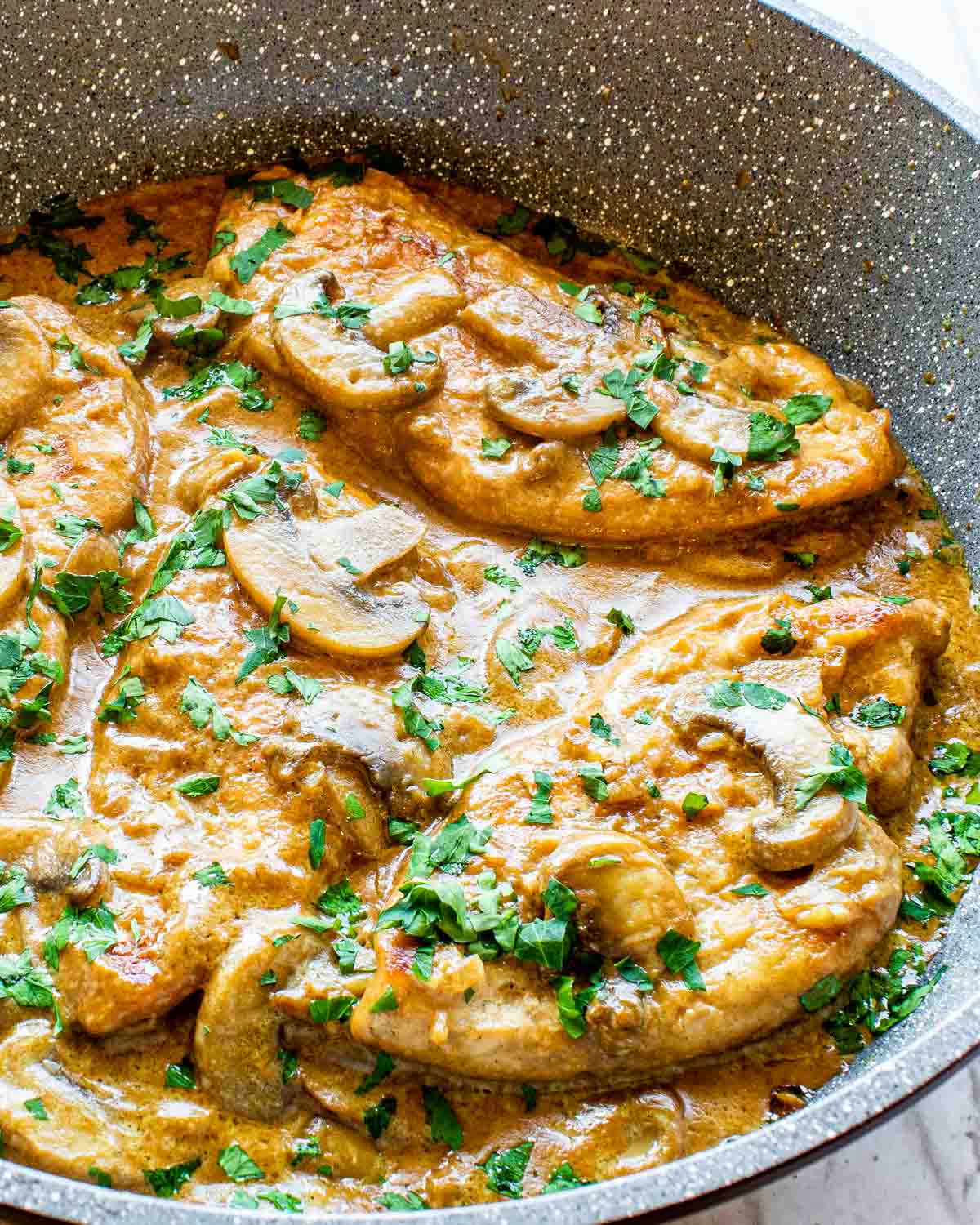 chicken marsala with mushroom sauce and garnished with parsley in a skillet.