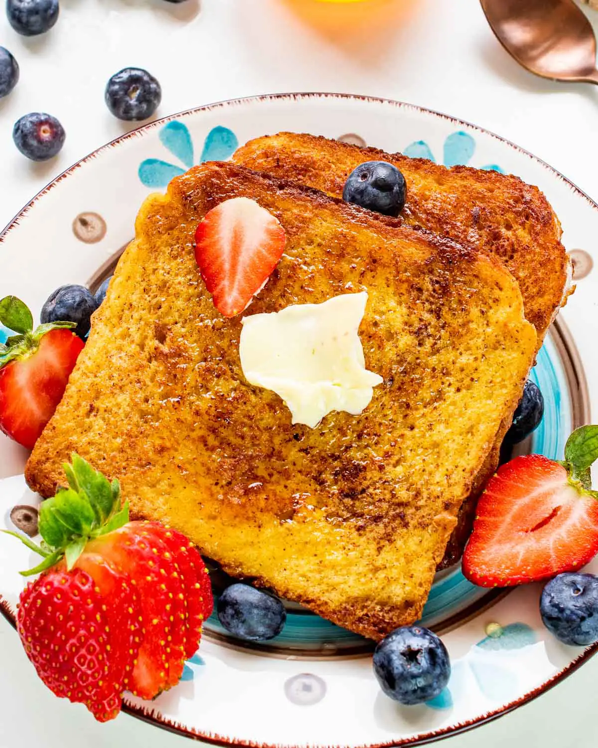 2 slices of french toast on a plate with butter and berries.