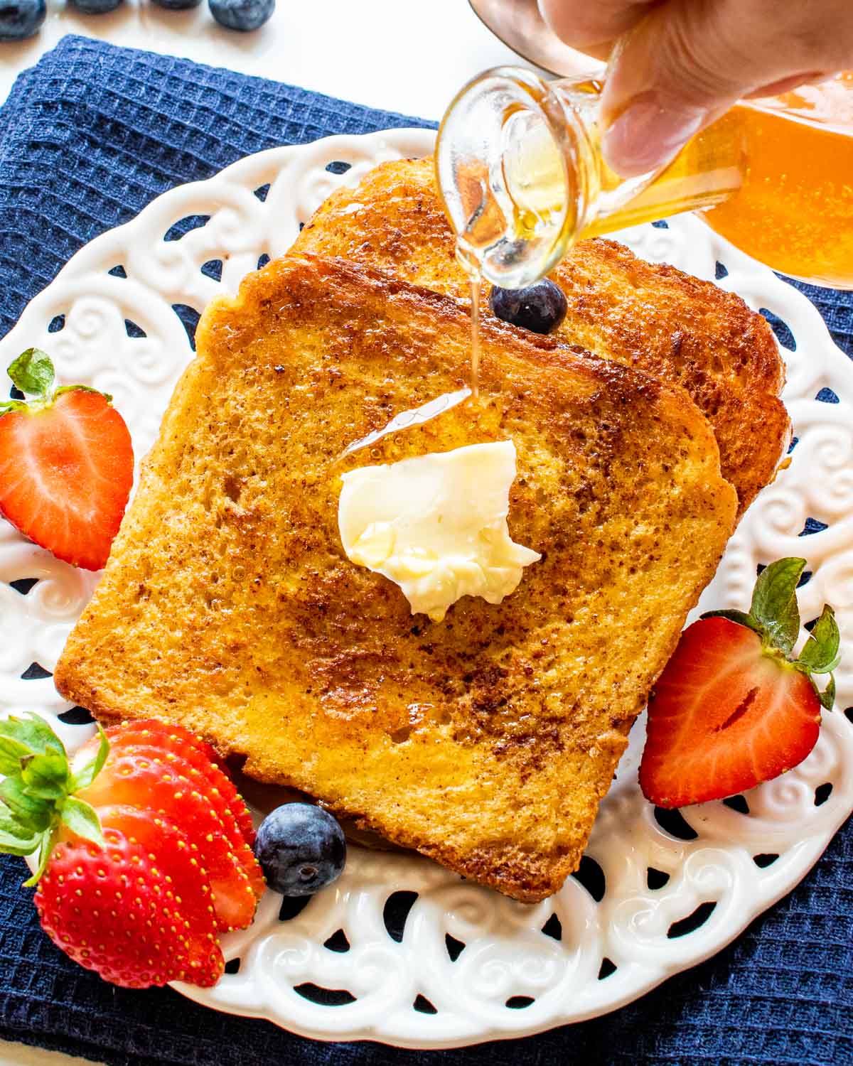 2 slices of french toast on a plate with butter and berries.