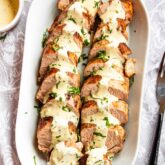 pork tenderloin sliced up with mustard sauce garnished with parsley on a white serving platter.