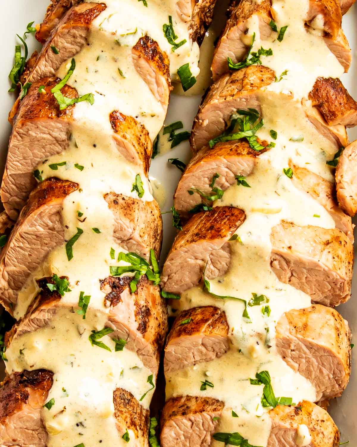 pork tenderloin sliced up with mustard sauce garnished with parsley on a white serving platter.