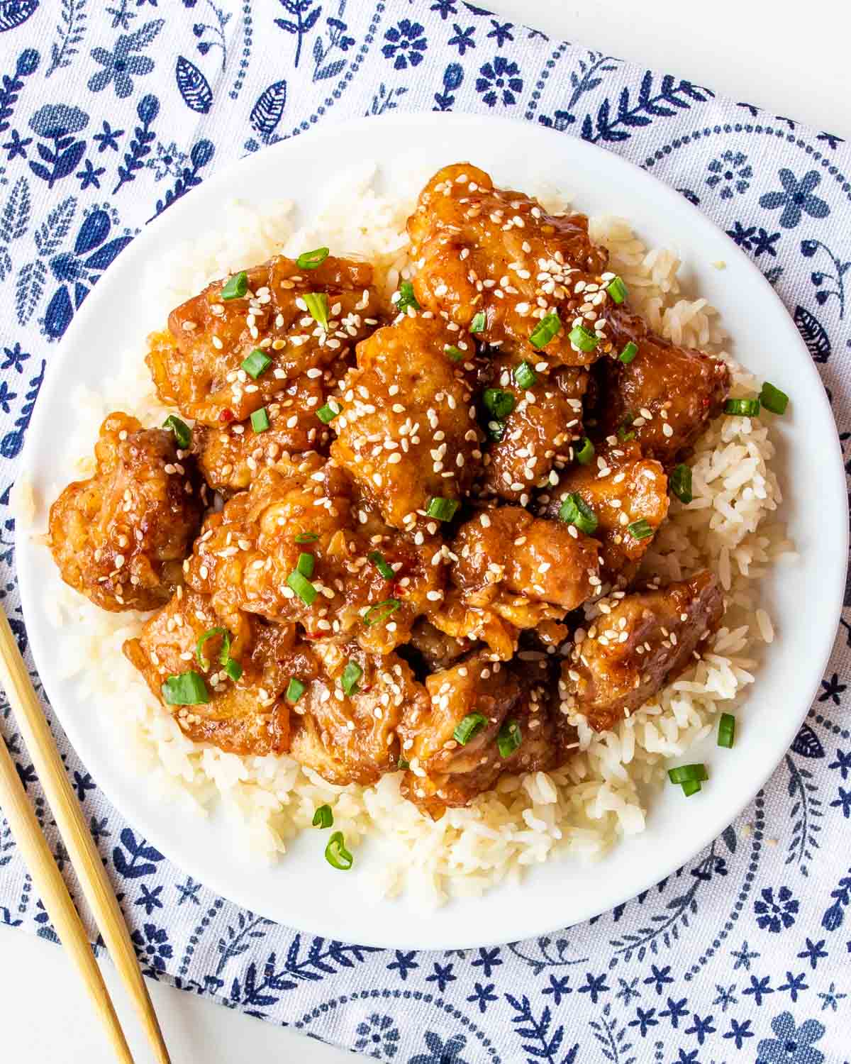 sesame chicken over cooked rice on a white plate.