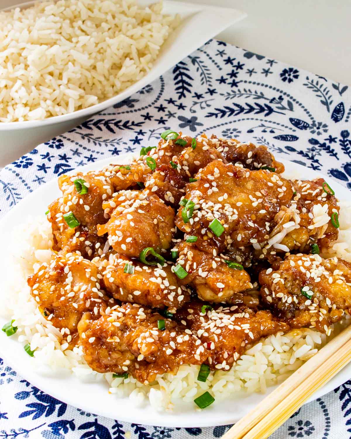 sesame chicken over cooked rice on a white plate.
