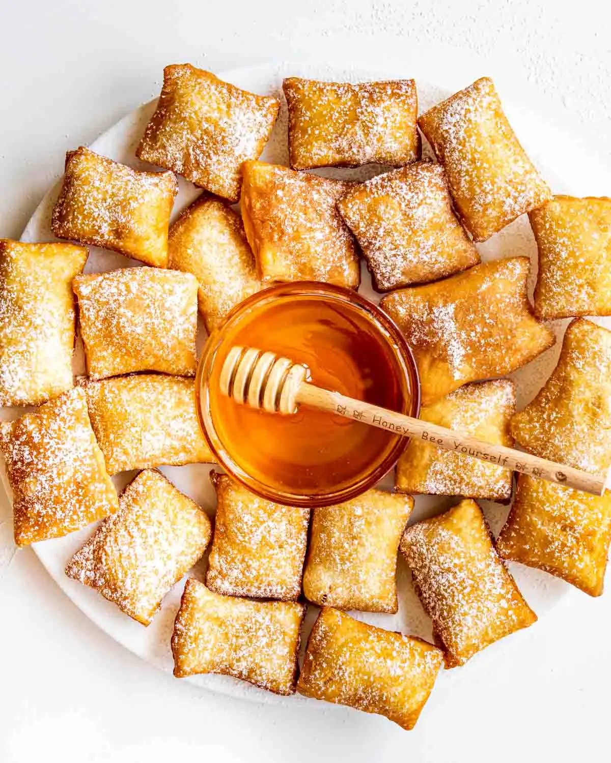 sopapillas on a big white plate with a bowl with honey in the middle.