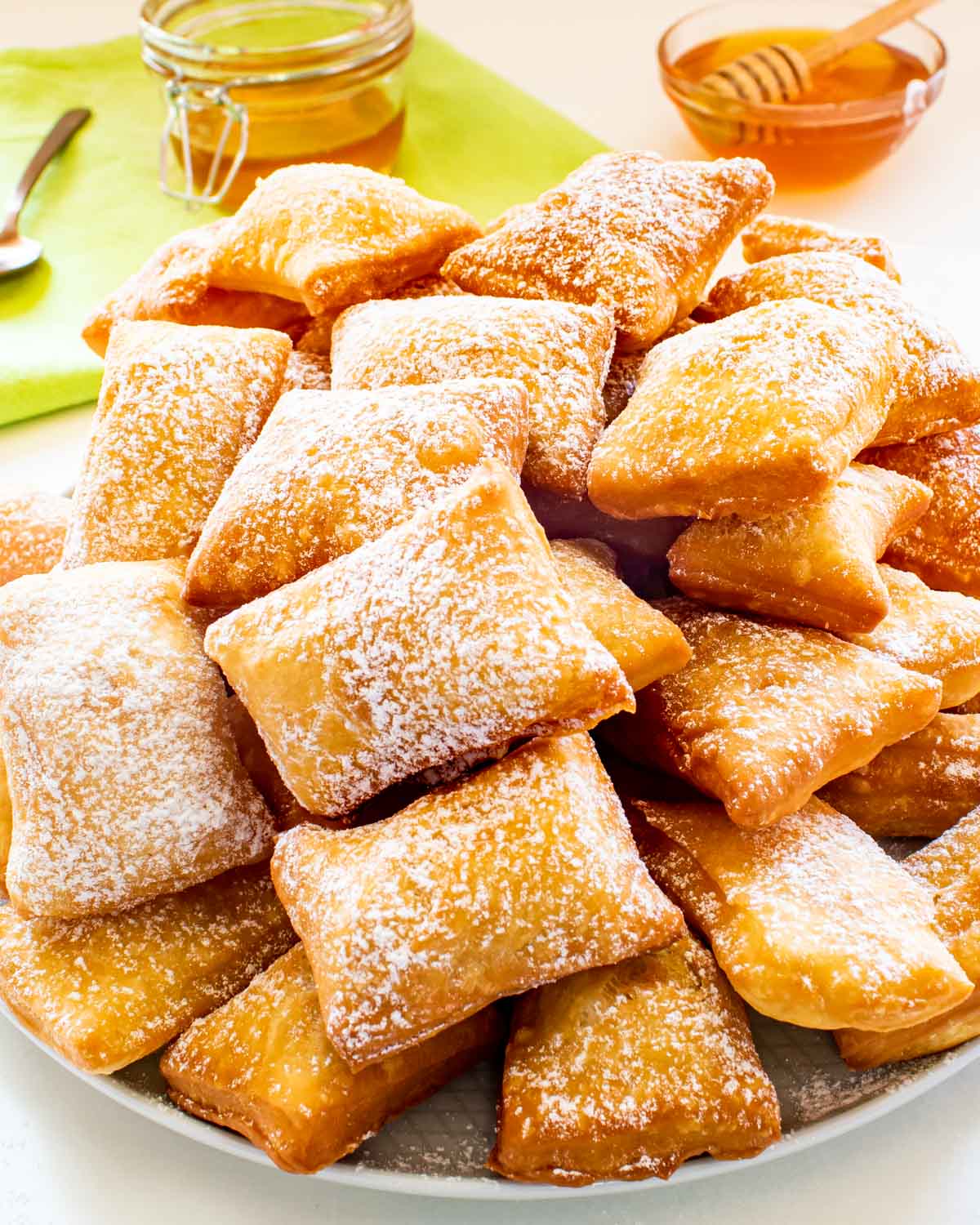 freshly fried sopappilas on a white plate sprinkled with powdered sugar.