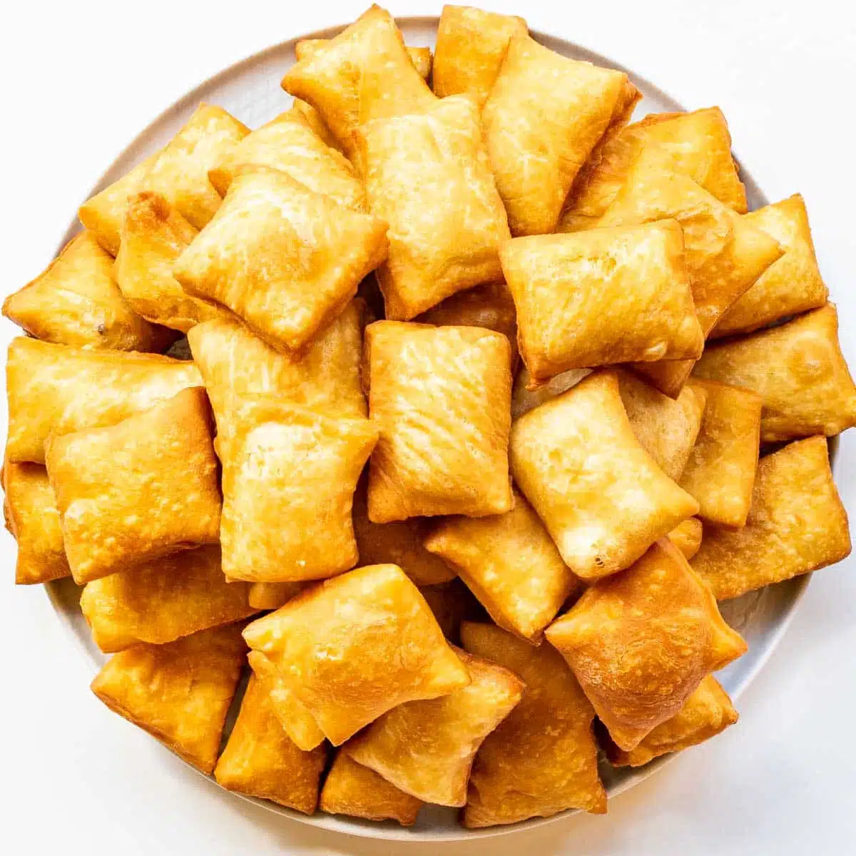 freshly fried sopapillas on a big white plate.