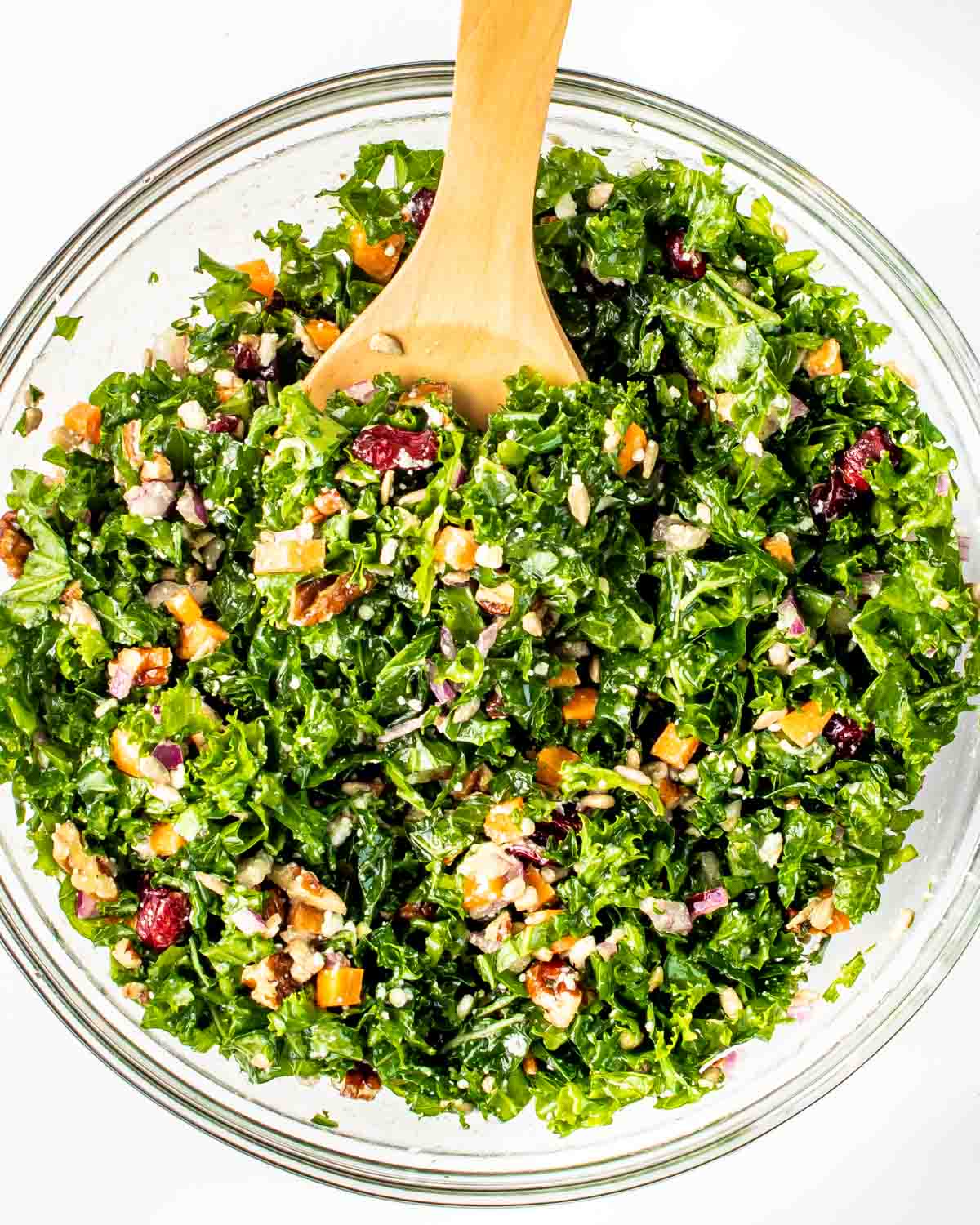 overhead shot of freshly made kale salad in a glass bowl with a wooden spoon inside.