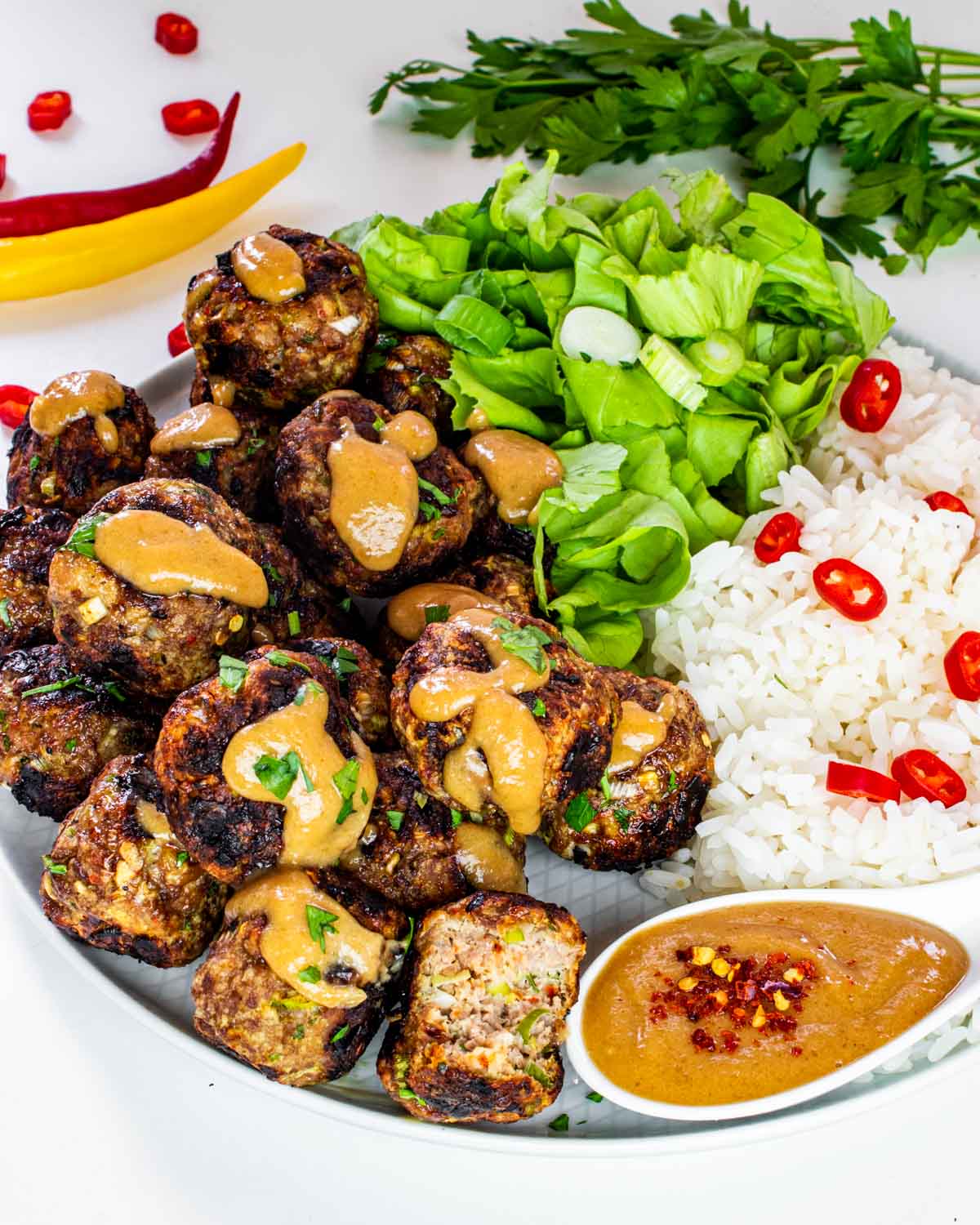 vietnamese meatballs with peanut sauce next to a bed of rice and garnished with thai red peppers.