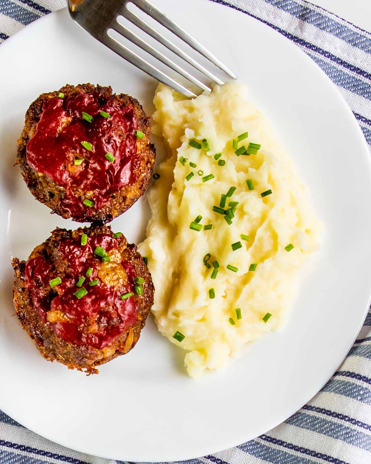2 meatloaf muffins on a plate next to a side of mashed potatoes.