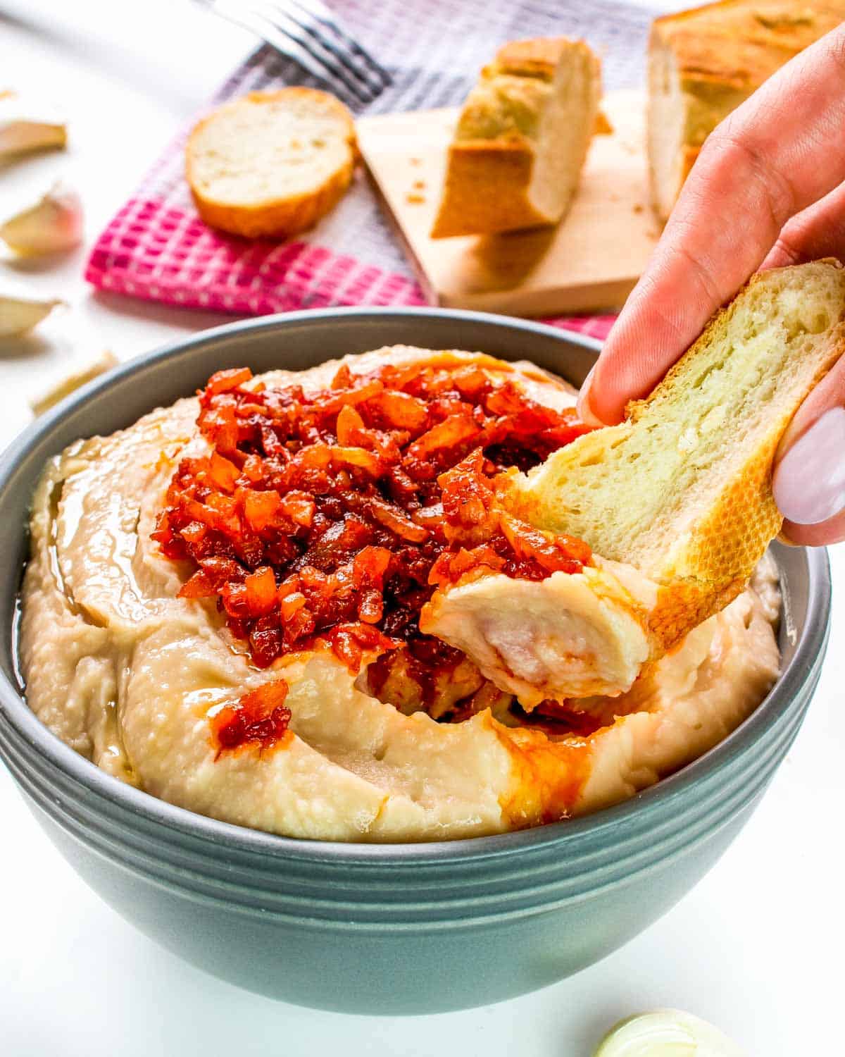 a hand dipping a piece of bread into a bowl with white bean dip.