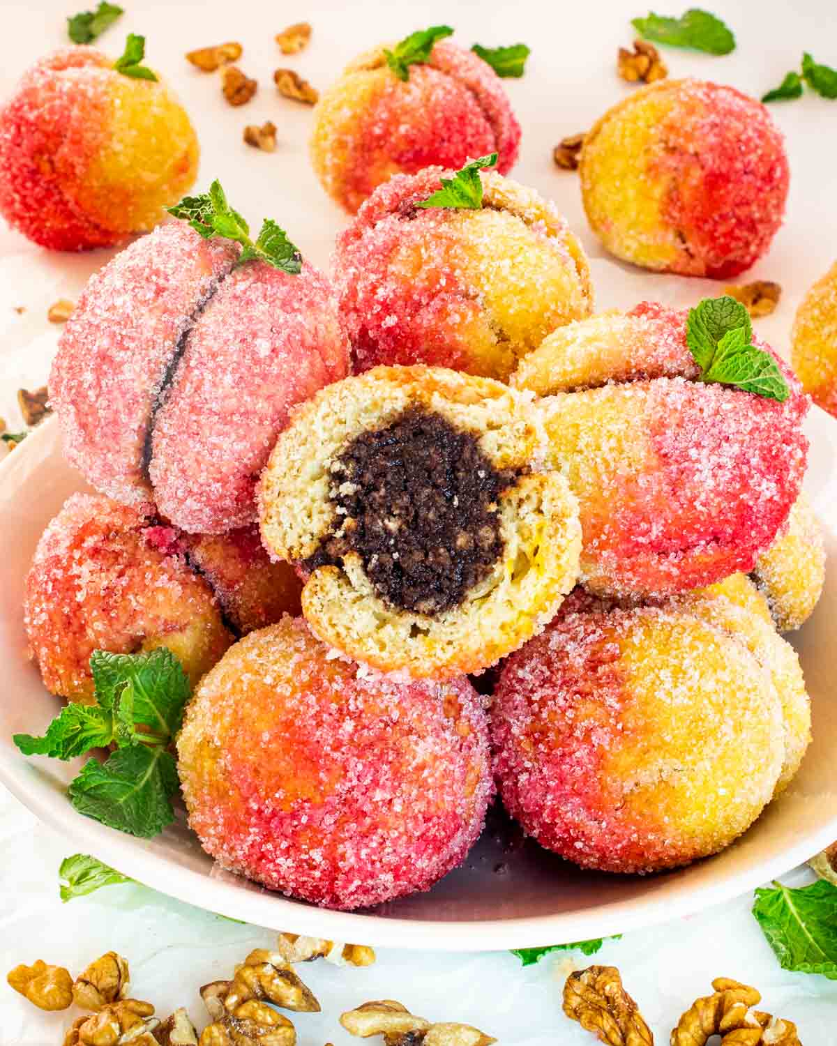 italian peach cookies on a plate with the top one cut in half.