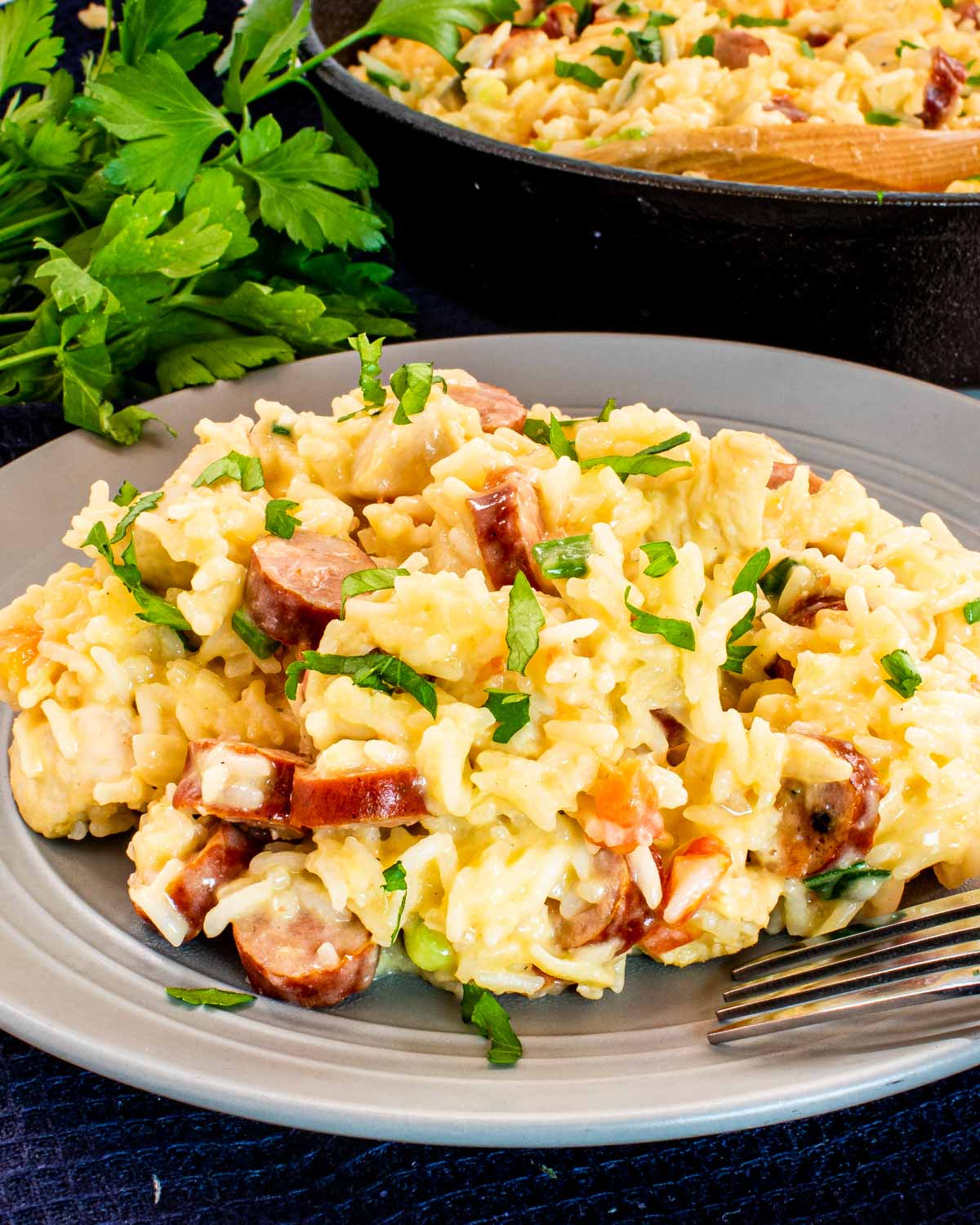 sausage chicken and cheesy rice in a plate garnished with parsley.