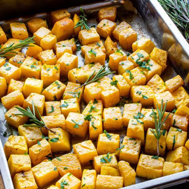 roasted butternut squash garnished in with rosemary and parsley in a pan.