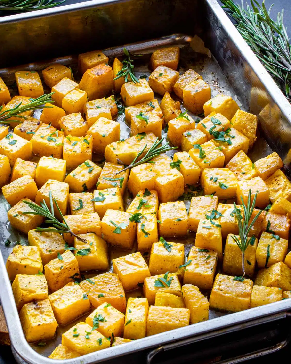 roasted butternut squash garnished in with rosemary and parsley in a pan.