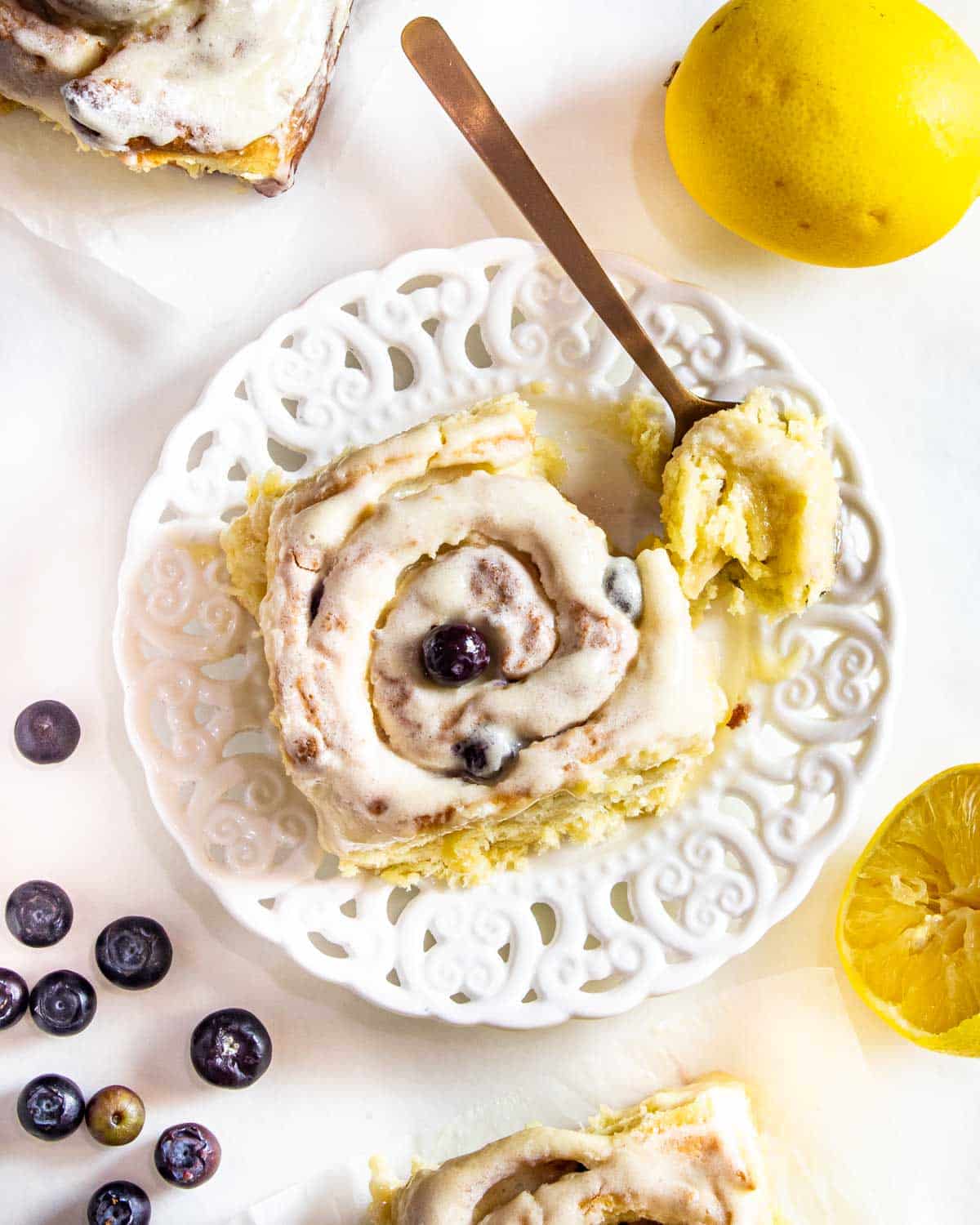 blueberry roll with cream cheese icing on a white plate with a spoon.