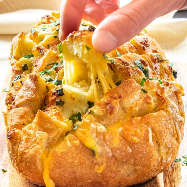 a head pulling a piece of cheesy bread from a pull apart bread.