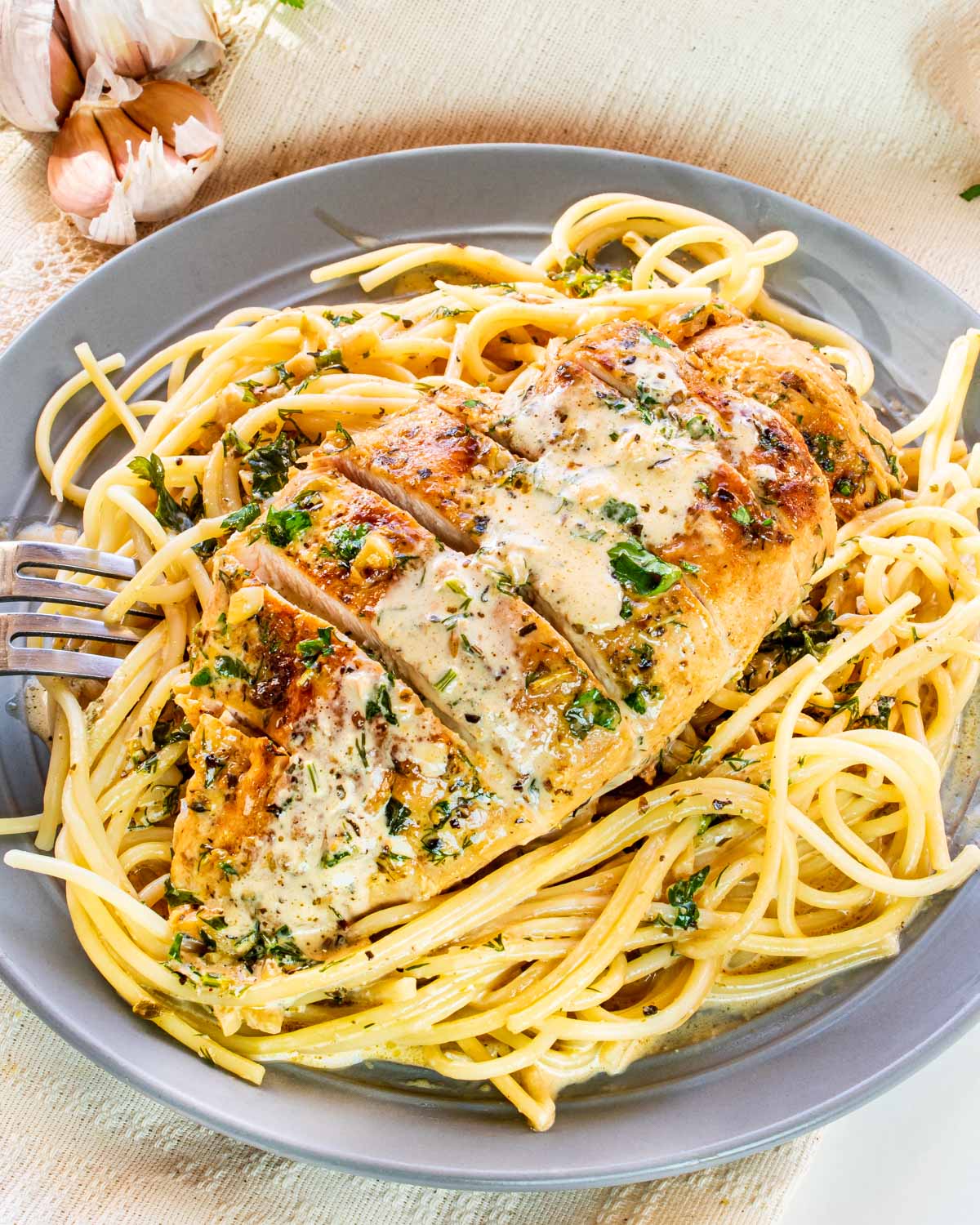 creamy herb chicken breast sliced up on a bed of spaghetti.