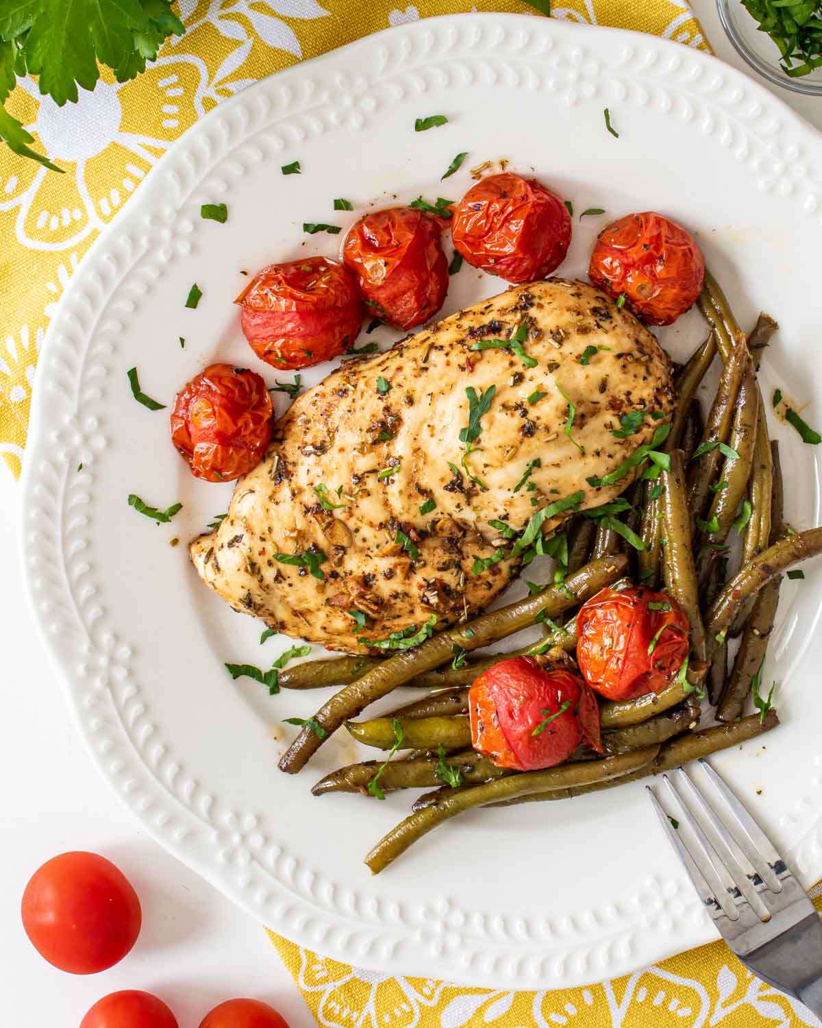 italian chicken breast with roasted green beans and tomatoes on a white plate.