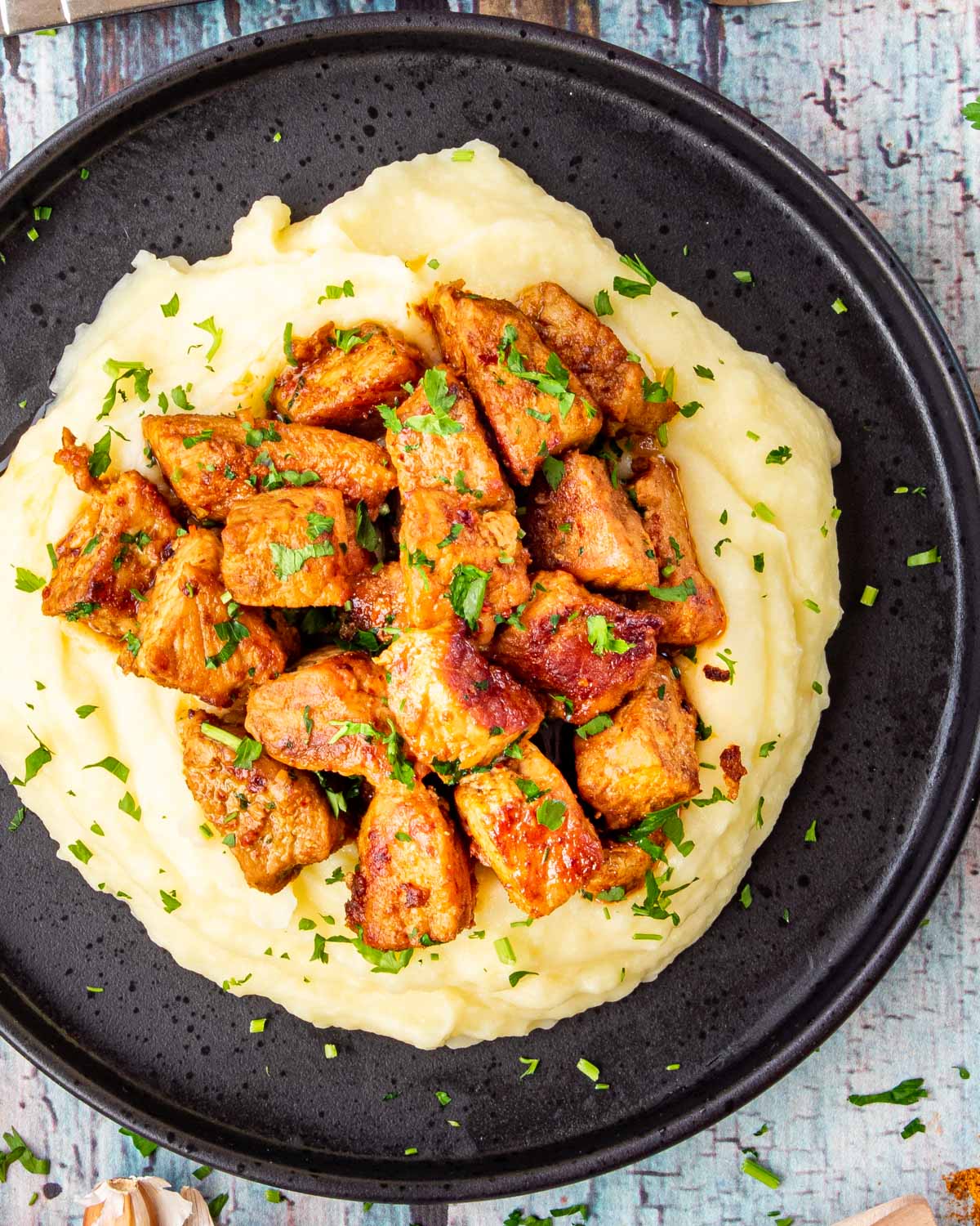 cajun pork bites on a bed of mashed potatoes on a black plate.